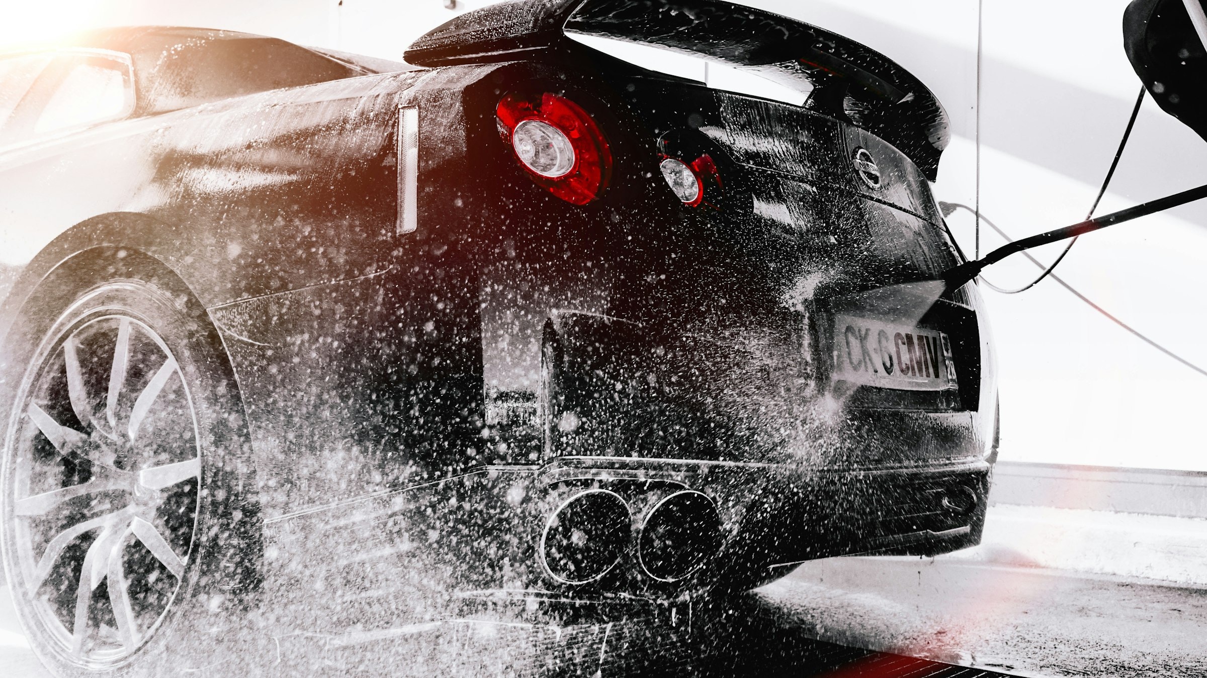 A black performance car being washed under high pressure — Carswells precision detailing in action
